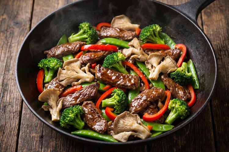 Beef stir-fry with broccoli, red bell pepper, snow peas, and oyster mushrooms in a black skillet.