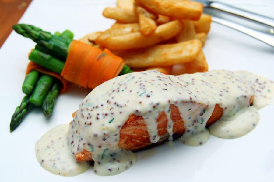 A dinner of salmon with seeded mustard and vegetables on a plate.