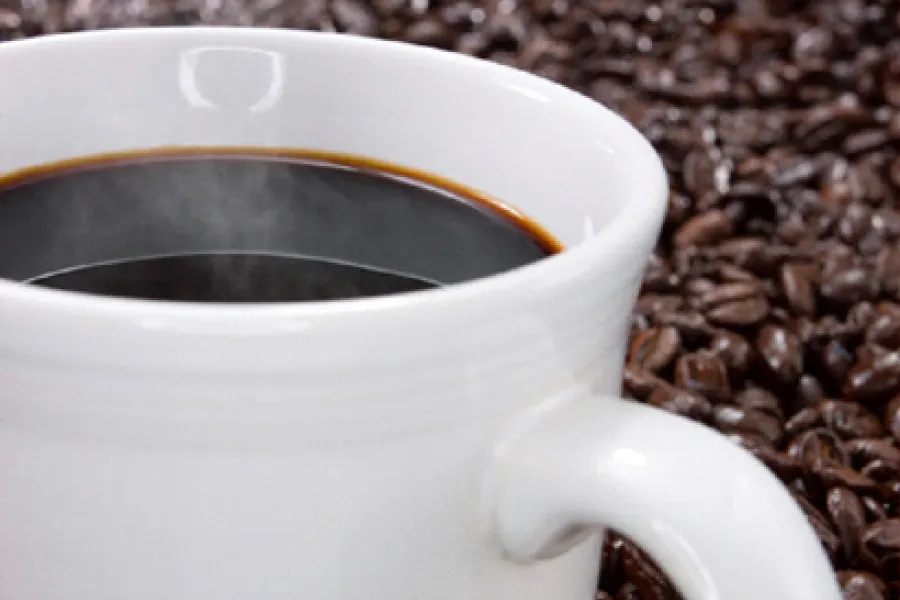 A cup with dark coffee with a background of roasted coffee beans.