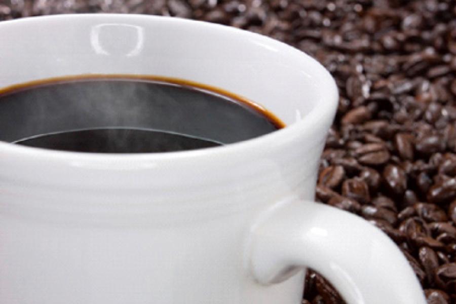 A cup with dark coffee with a background of roasted coffee beans.
