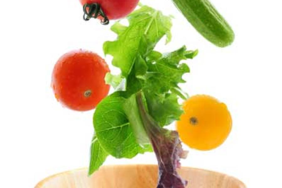 Salad ingredients falling into a wooden salad bowl.