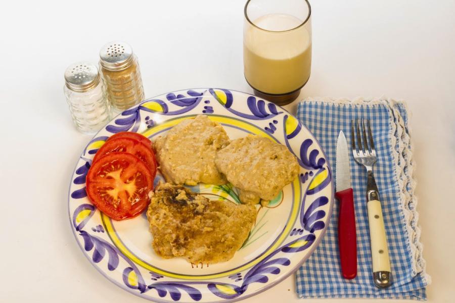 A plate with pork chops, biscuits and gravy with a glass of milk on the side.