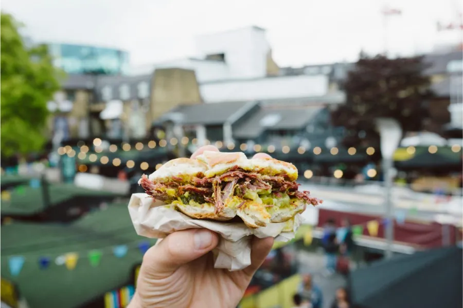 A hand holding a sandwich from a street food stall.