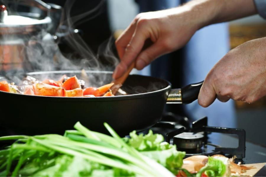 A cook prepares a base for a stew in a pan.