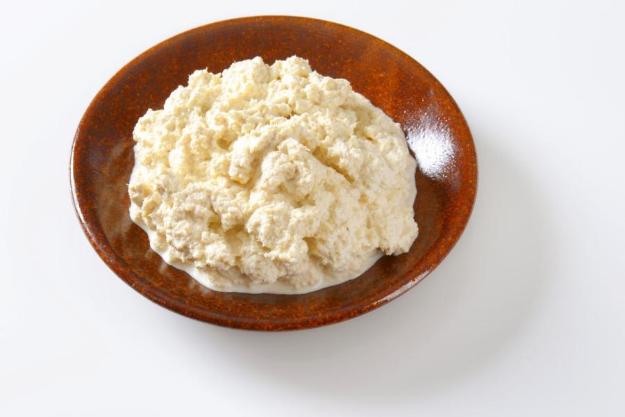 Brown ceramic bowl filled with creamy, chunky horseradish sauce on a white background.