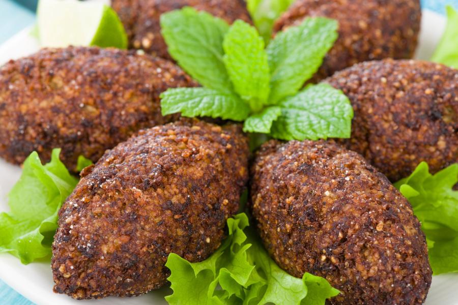 Plate of elongated, fried kibbeh garnished with fresh mint leaves and surrounded by lettuce leaves.