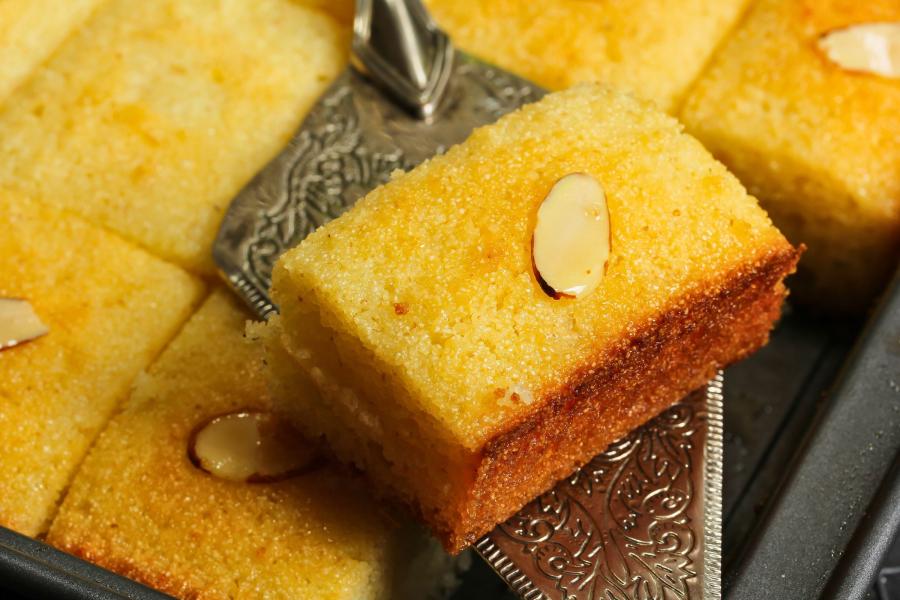 Close-up of semolina cake pieces topped with almond slivers on a tray with a decorative silver cake server.
