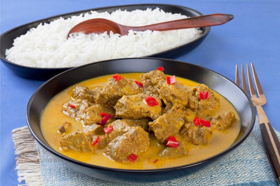 A bowl of beef Madras curry with a creamy yellow sauce and red chili pepper garnish, served alongside a bowl of white rice.