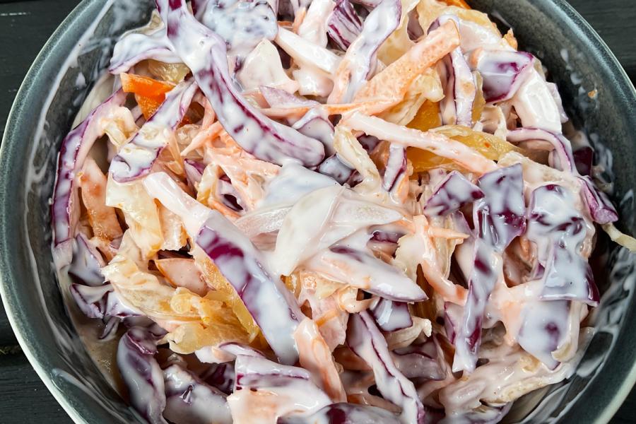 A bowl of kimchi coleslaw featuring shredded red cabbage, kimchi mixed with carrot and onion, coated in a creamy dressing