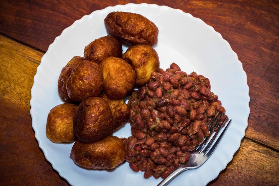 A plate of golden-brown puff-puff, or fried dough balls, served with seasoned red beans, a traditional West African dish, on a white plate with a fork resting on the side.