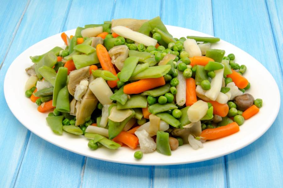Suggested alt text:** "A plate of vegetable menestra with peas, carrots, green beans, artichokes, and asparagus, on a blue wooden surface.