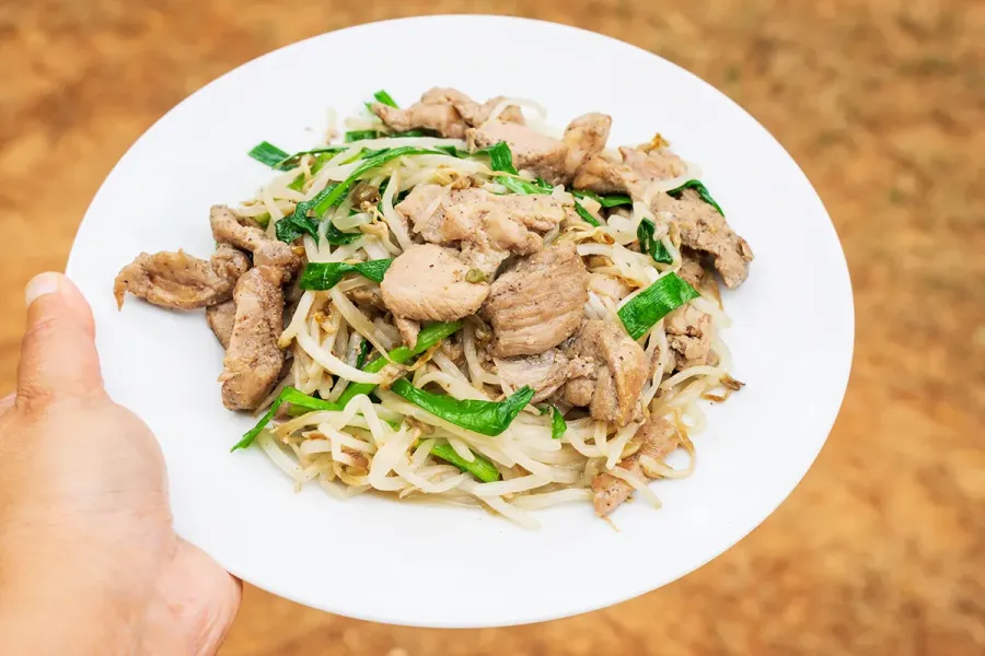 A plate of Vietnamese stir-fried pork with bean sprouts and garlic chives, showcasing tender pork slices mixed with crisp bean sprouts and green chives.