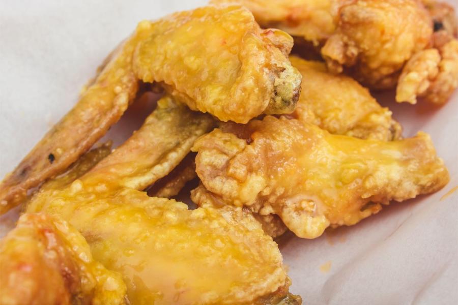 Close-up of crispy chicken wings coated with a glossy citrus glaze, showcasing a golden-brown crust and a sticky yellow-orange finish.