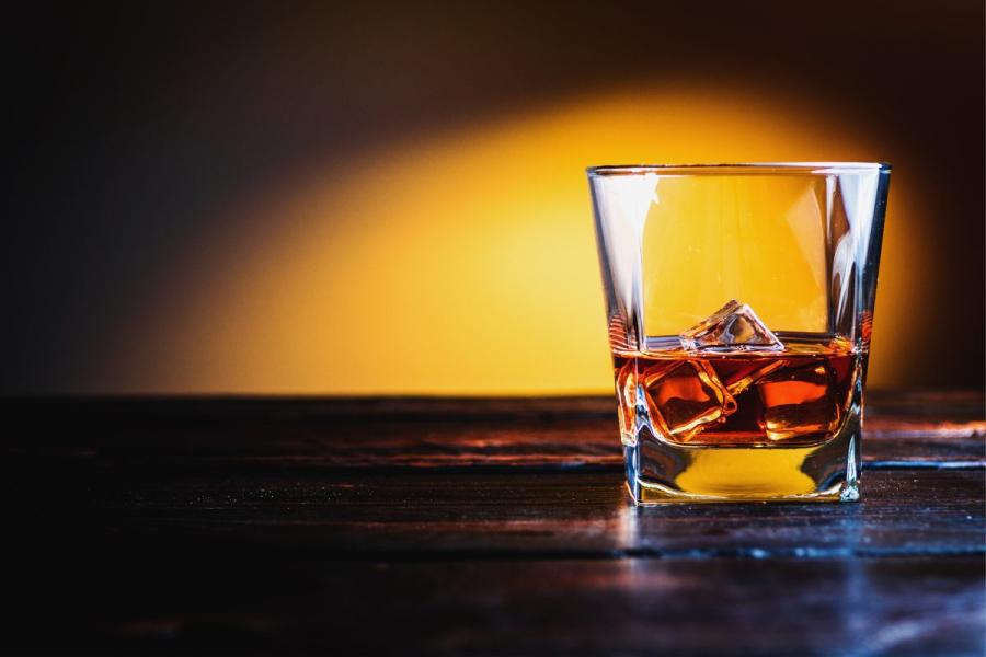 Bourbon with ice cubes on darke wood table and orange background.