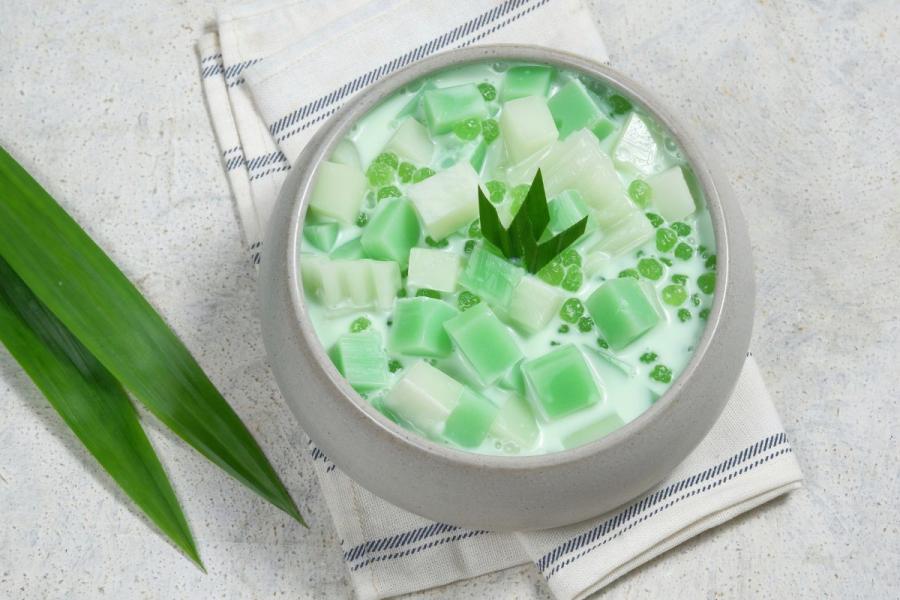 A bowl with buko pandan salad with a couple of pandan leaves on the side, top view.