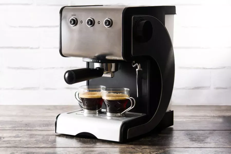 Modern espresso machine brewing two shots of espresso into glass cups on a wooden surface with a white brick wall background.