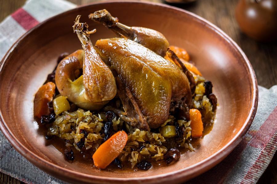 Stewe squab with cabbage, raisins and carrot plated in a stoneware dish.