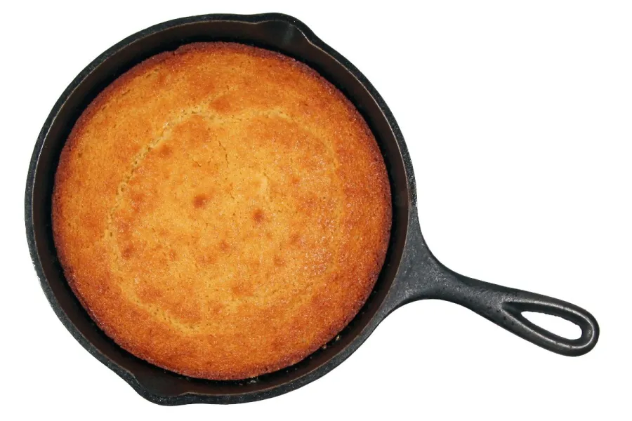 Golden-brown cornbread baked in a cast-iron skillet on a white background.