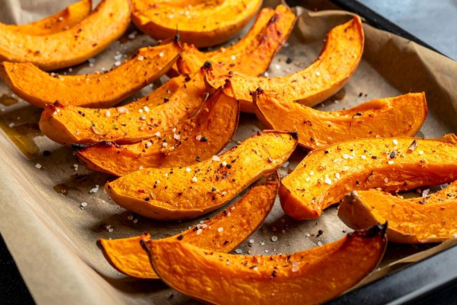 Roasted butternut squash wedges on a parchment-lined baking tray, sprinkled with salt and pepper.