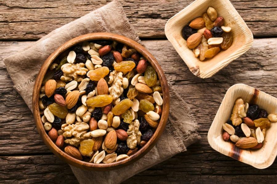 A close-up, top-down view of a rustic wooden bowl brimming with a healthy mix of nuts and dried fruit.
