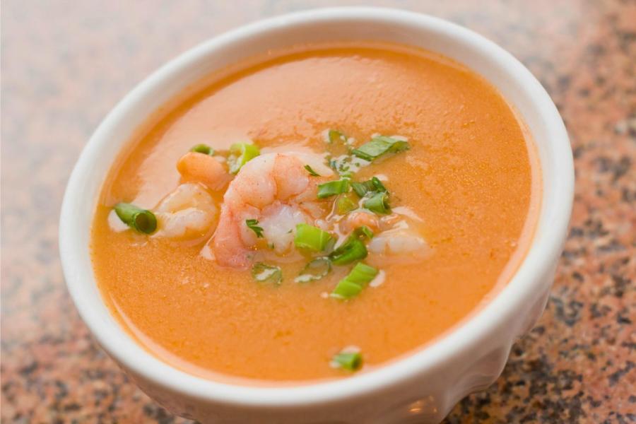 A bowl of prawn bisque garnished with whole prawn tails and chives.