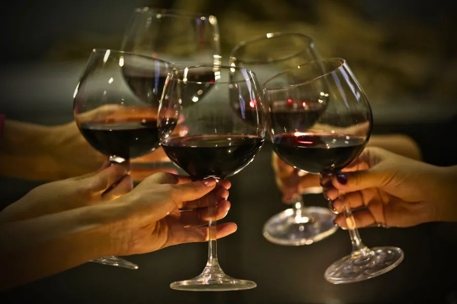 Four people share a toast and clink wine glasses filled with red wine.