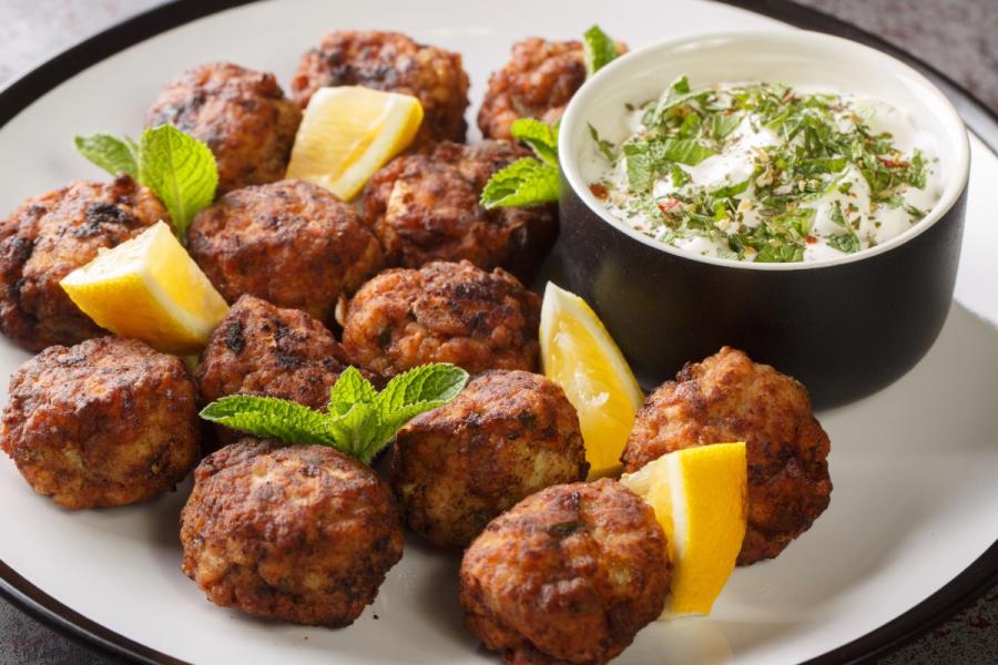 A white plate with fried keftedes, Greek veal meatballs, served with tzatziki and pieces of lemon.