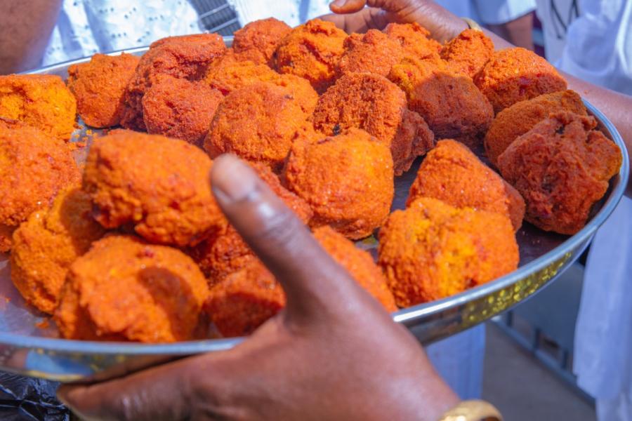 Hands hold a tray piled with orange-red fried akara.