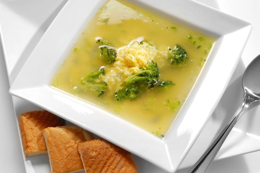Bowl of sopa de huevo with broccoli in light broth, served with bread.