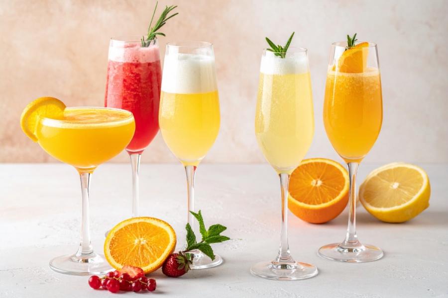 Five colorful wine cocktails in stemmed glasses with citrus, berry, mint, and rosemary garnishes on a light tabletop.