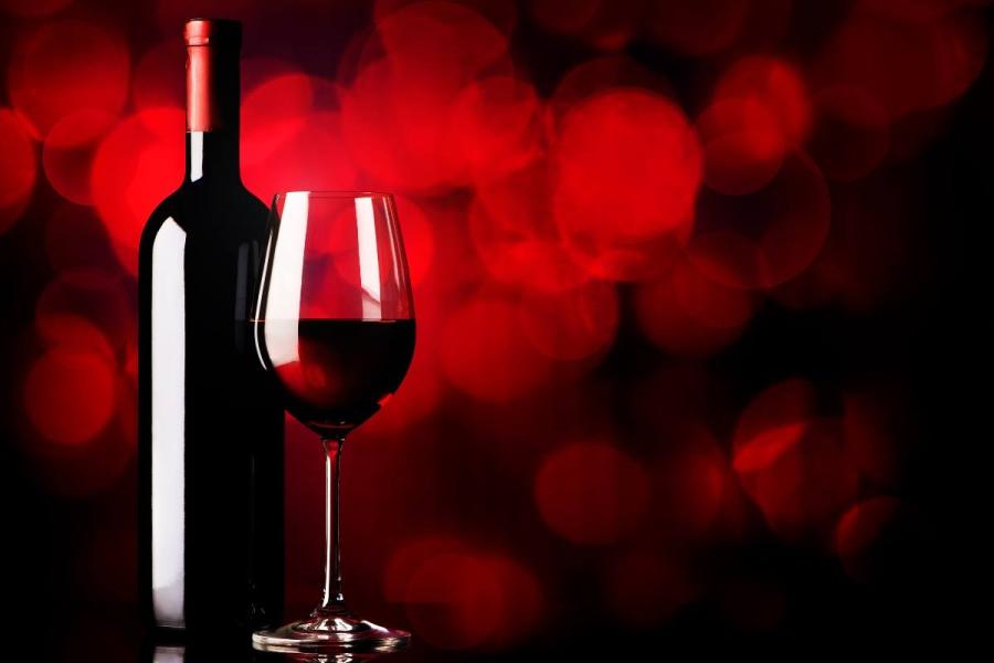 Bottle of fortified red wine beside a filled wine glass against a dark red bokeh background.