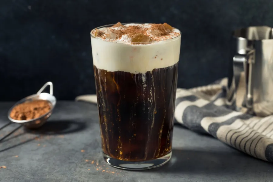 all glass of iced Einspänner topped with whipped cream and cocoa powder on a dark countertop with café-style background props.