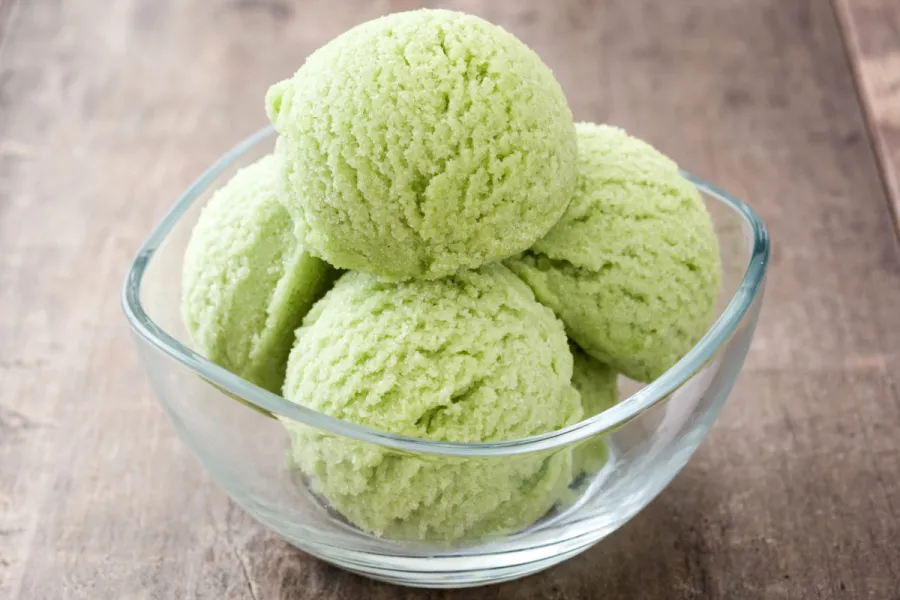 Four scoops of matcha ice cream in a glass bowl with a square rim.