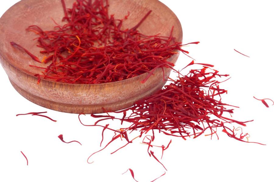 Red saffron threads in a wooden bowl with some spilled on a white background.
