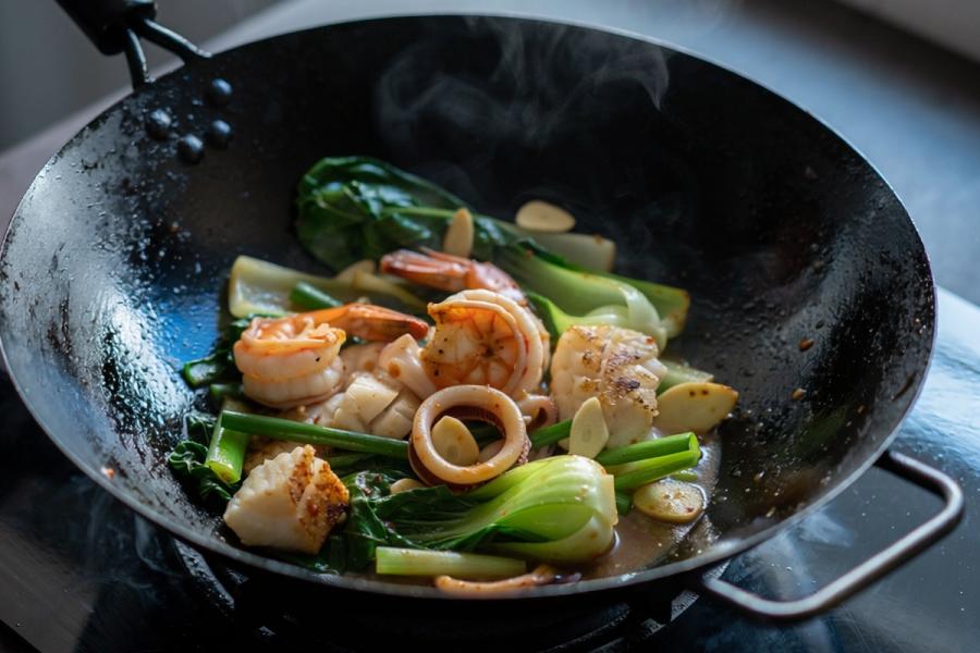 A wok of stir-fried shrimp, scallops, squid rings and white fish with Asian greens and garlic, glistening in a savory sauce, with steam rising.