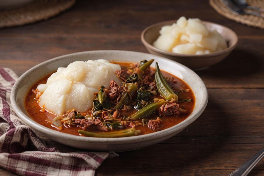 Bowl of Angolan calulu, shredded dried meat with okra and greens in a red palm-oil broth, served with a mound of white funge