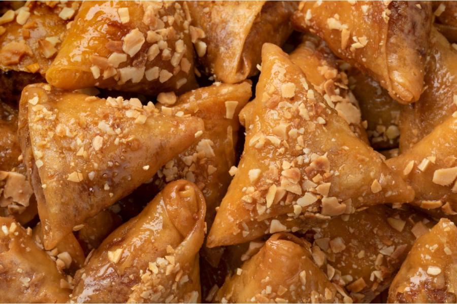 A close-up of golden Moroccan almond briouats, crisp phyllo triangles glazed with honey and scattered with chopped almonds, piled together