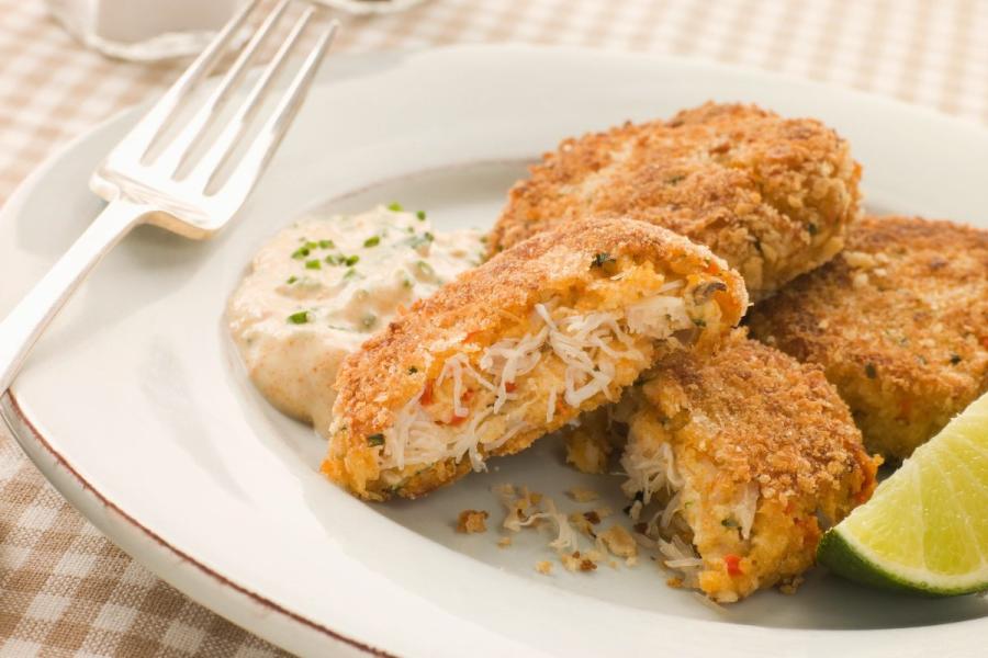 Freshly baked golden brown Maryland crab cakes on a white plate garnished with lemon wedges and tartar sauce.