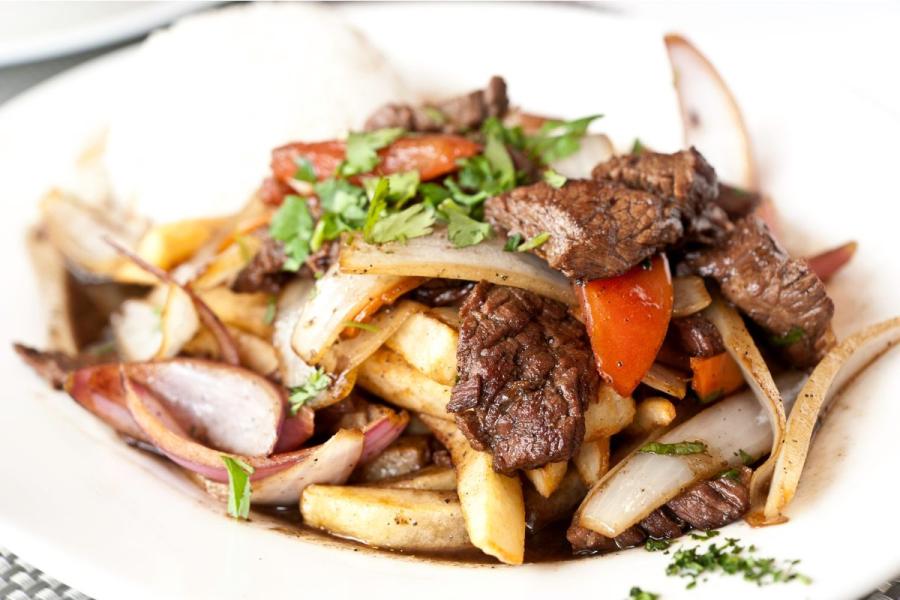 A plate with sitr fried meat and vegetables with soy sauce and liquied known as Peruvian lomo saltado.