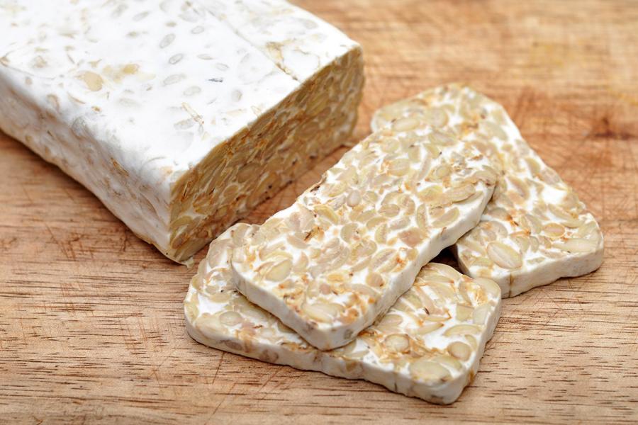 Some sliced fresh tempeh and a cake on a wooden cutting board.
