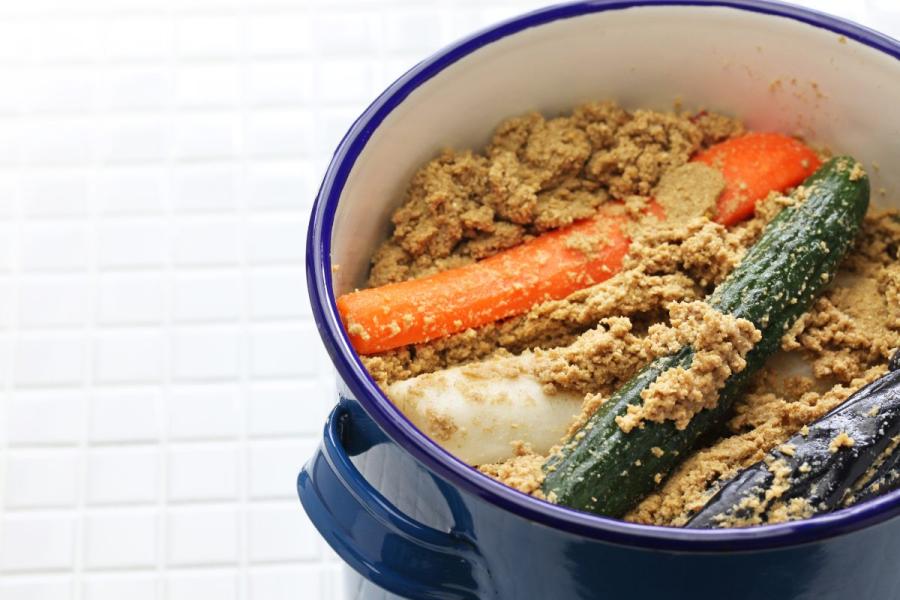 Assorted nukazuke vegetables, including radishes, cucumbers, carrots, and cabbage, arranged in a deep blue porcelain-coated pan.