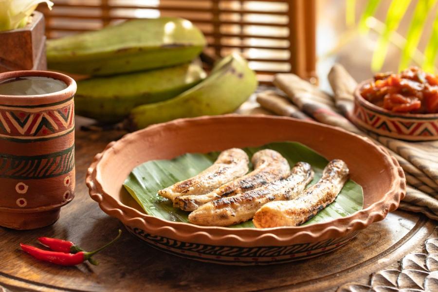 Boli over a banana leaf in a plate with spiciy sauce on the side.