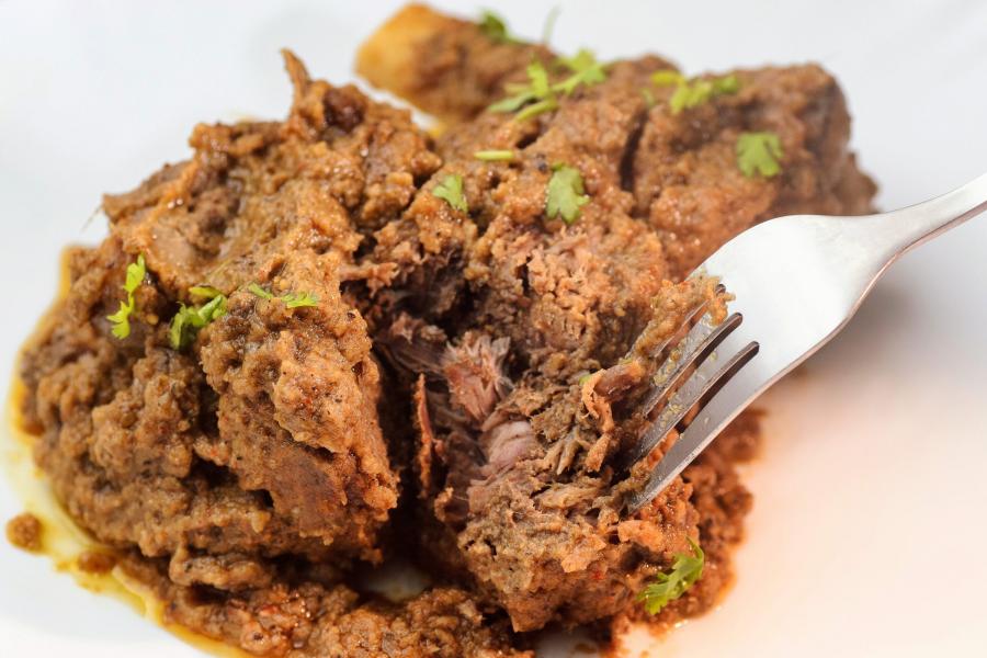 Tender slow cooked lamb raan with thick brown gravy and green garnish and a fork.
